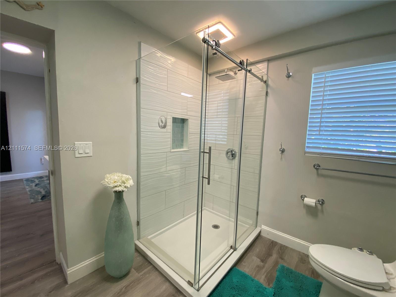 Glass-enclosed shower with textured wall tile and built-in recessed niche, complemented by wood-finish flooring and wall-mounted metal hardware