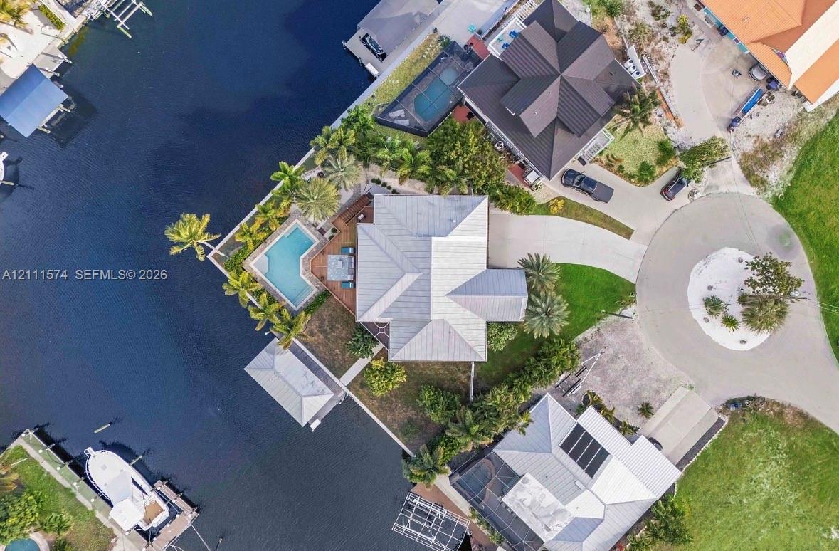 Waterfront property featuring a private swimming pool, concrete boat dock, and a paved circular driveway