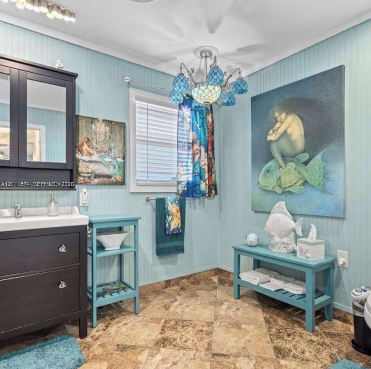 Bathroom featuring beadboard wall paneling, a dark wood-finish vanity with a rectangular sink, multi-tone tile flooring, and a decorative multi-arm chandelier