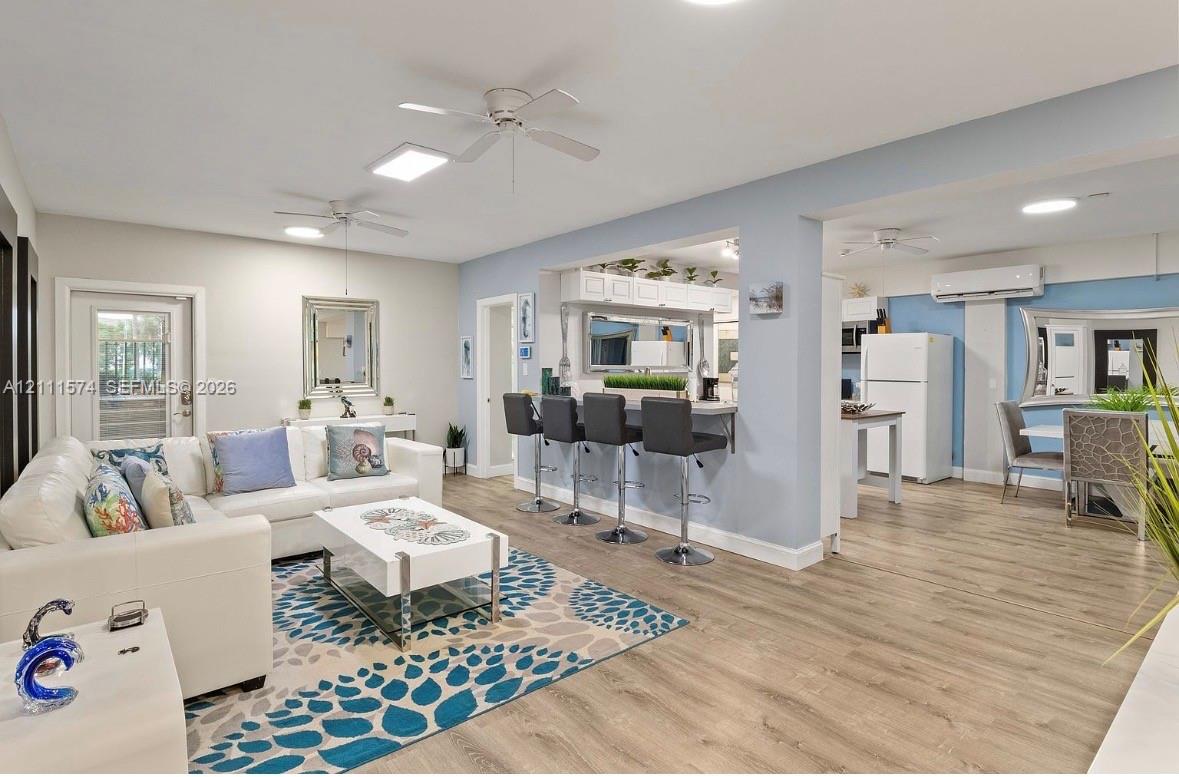 Open-concept interior featuring wood-finish flooring, a kitchen pass-through counter, ceiling fans, and a ductless mini-split system