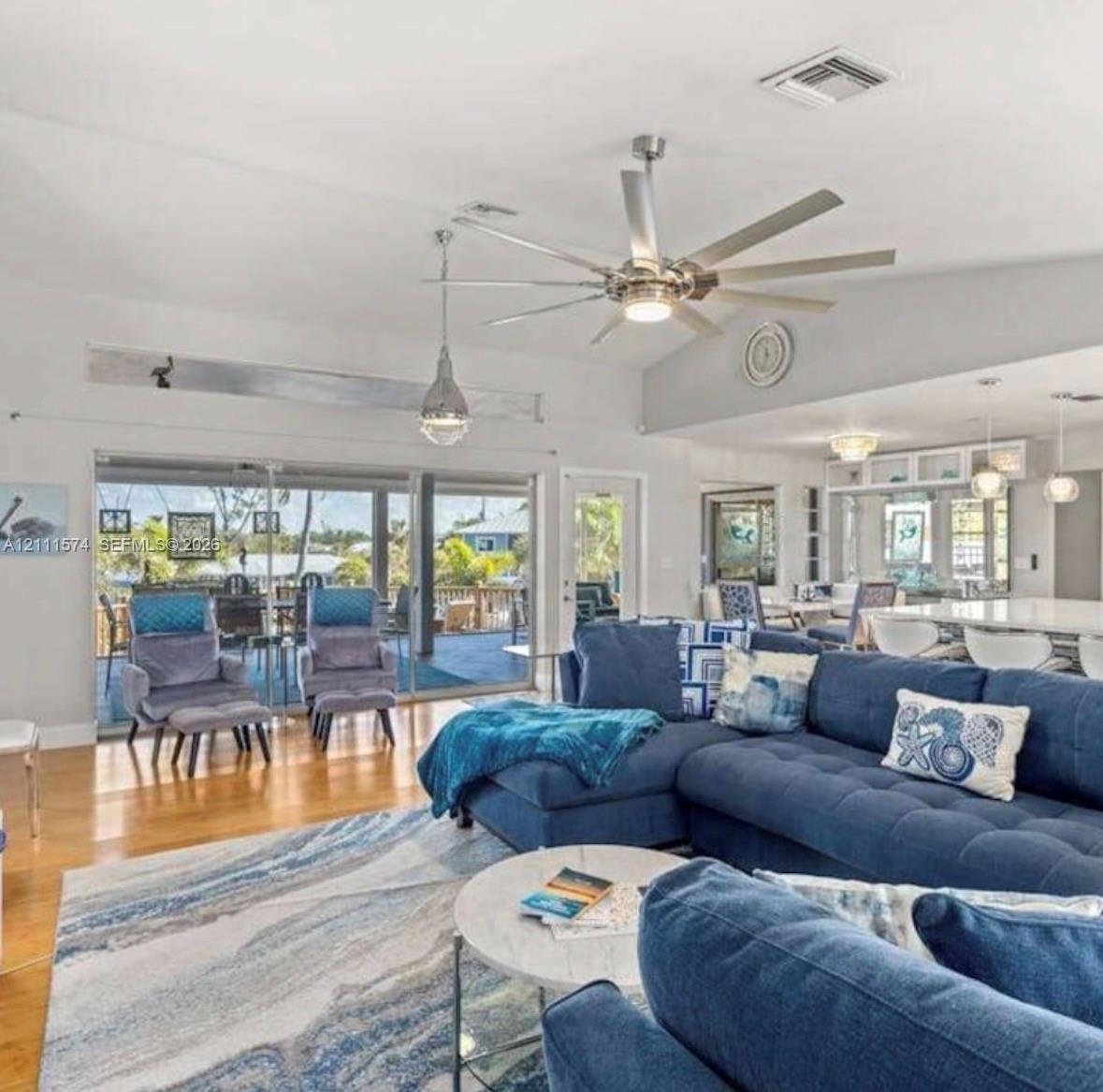 Vaulted ceilings featuring a multi-blade brushed nickel ceiling fan with integrated lighting, wood-finish flooring, and expansive sliding glass doors