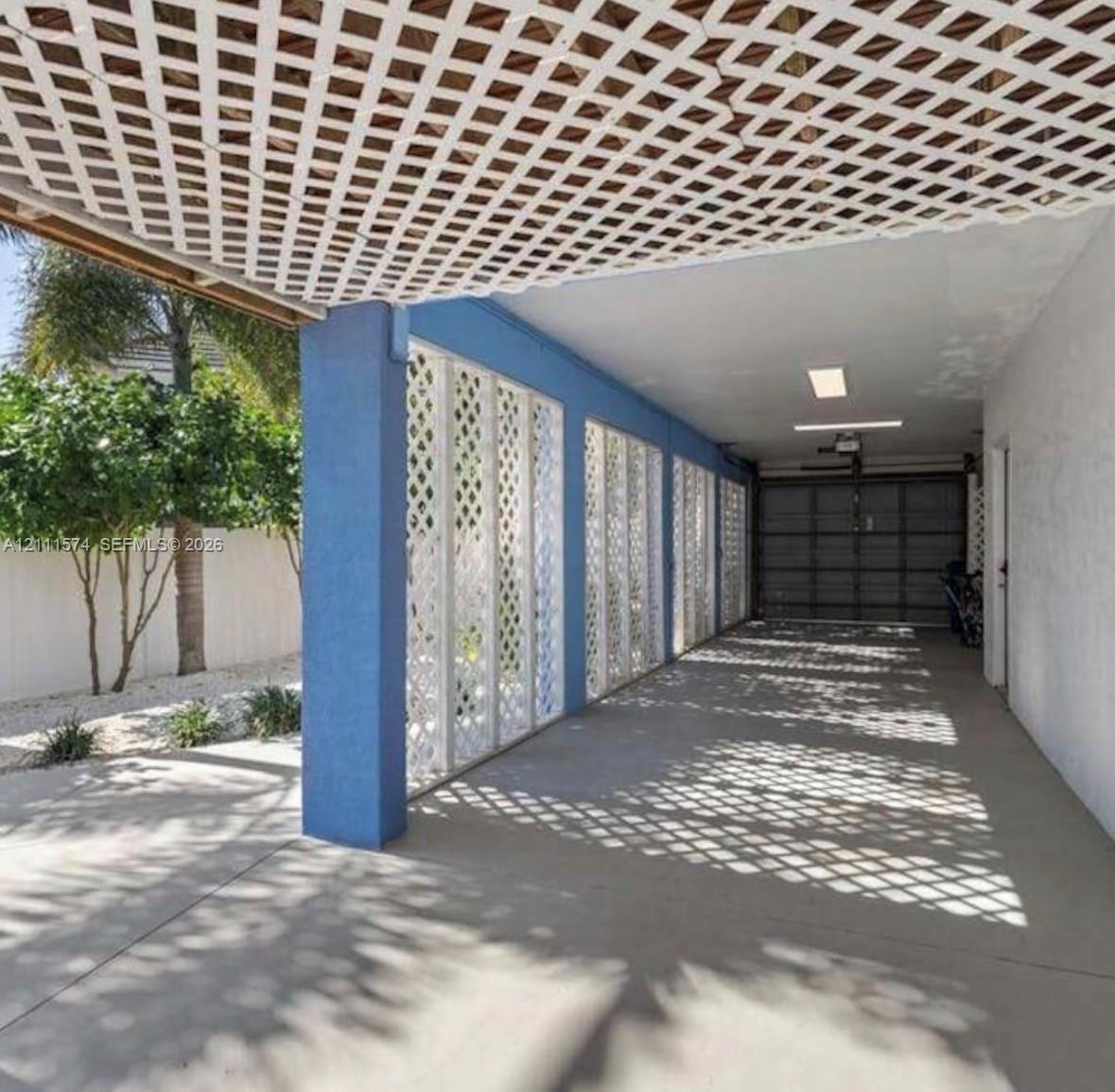 Covered carport featuring a concrete floor, lattice privacy screening, and recessed lighting, with a side door and an attached garage door