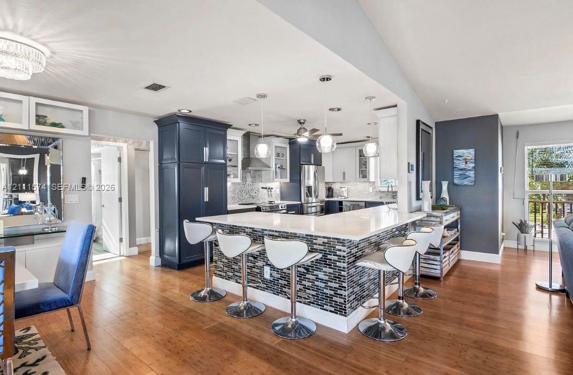 Kitchen featuring custom navy and white cabinetry, stone-finish countertops, multi-tonal mosaic tile breakfast bar, pendant lighting, and wood-finish flooring