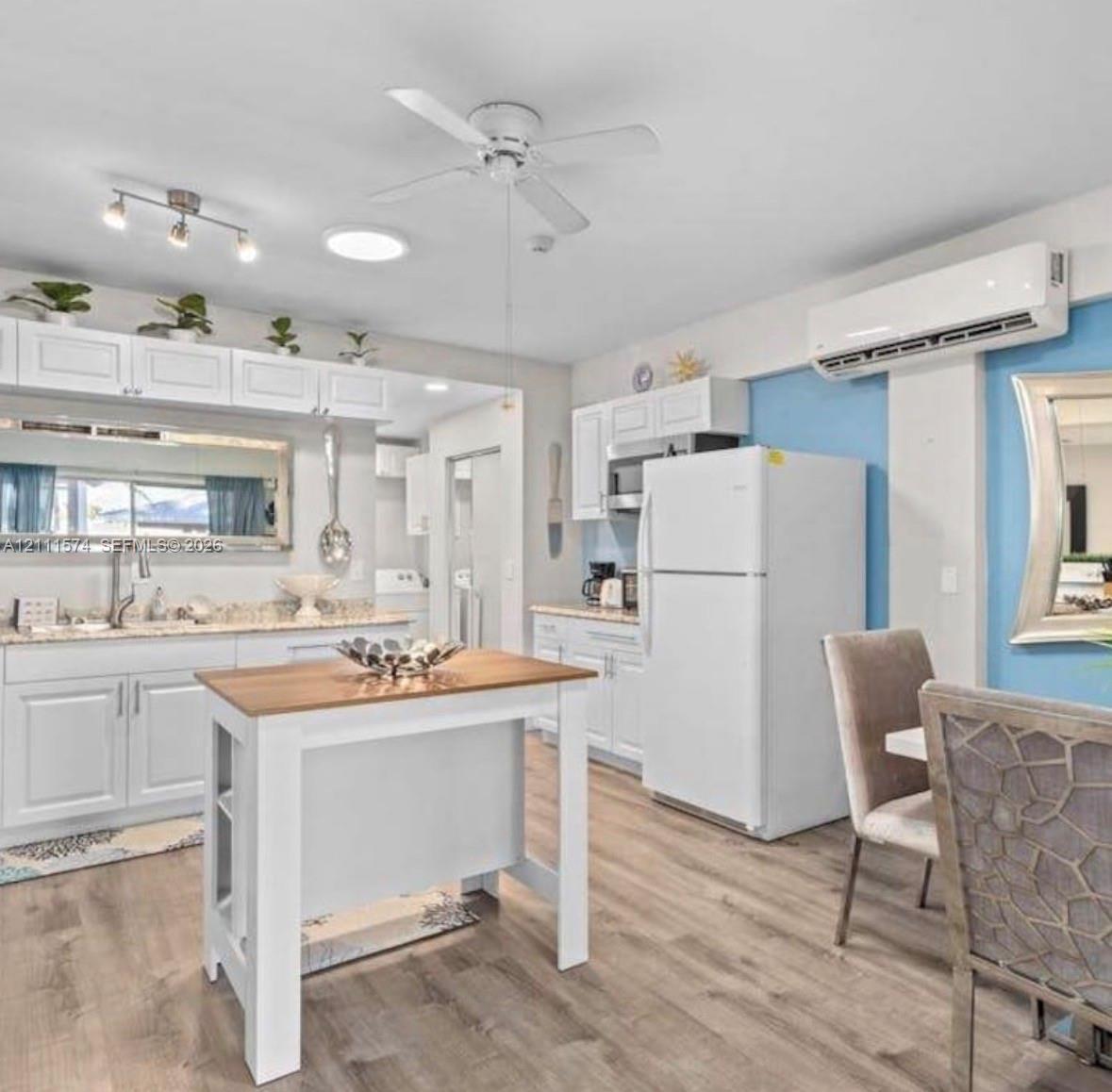 Kitchen featuring white cabinetry, stone-finish countertops, wood-finish flooring, a ceiling fan, and a wall-mounted ductless air conditioning unit
