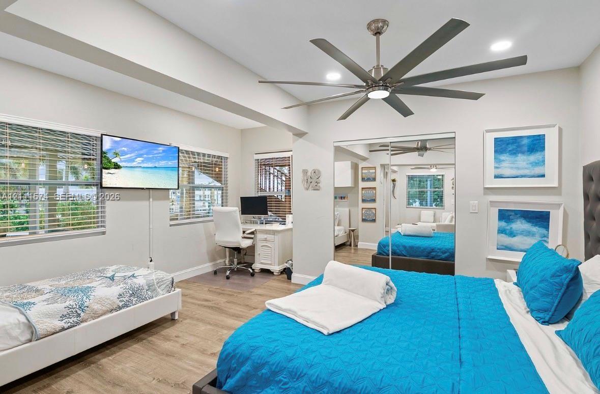 Tray ceiling, wood-finish flooring, multi-blade ceiling fan, and mirrored sliding-door closet