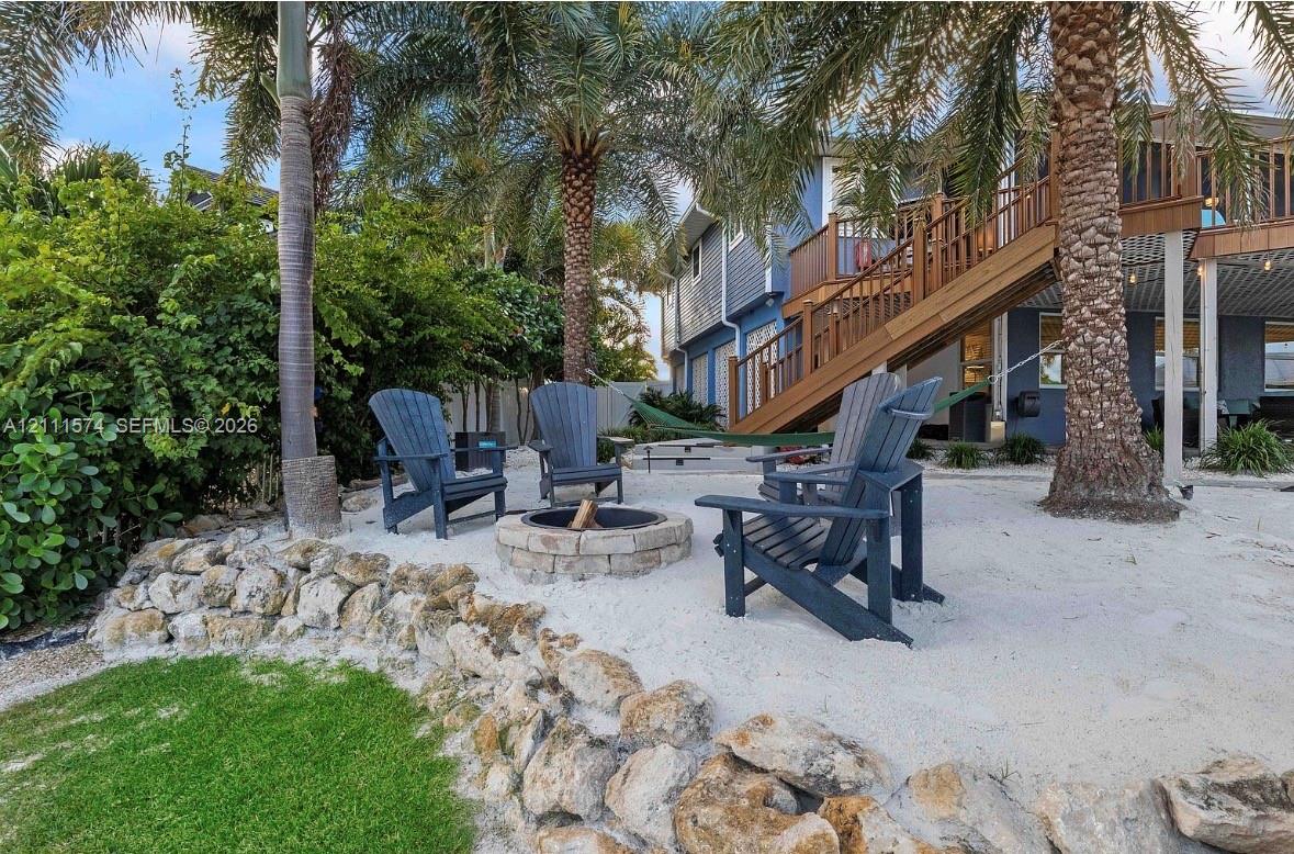 Backyard featuring a sand-ground fire pit, stacked stone retaining wall, mature palm trees, and a wooden exterior staircase