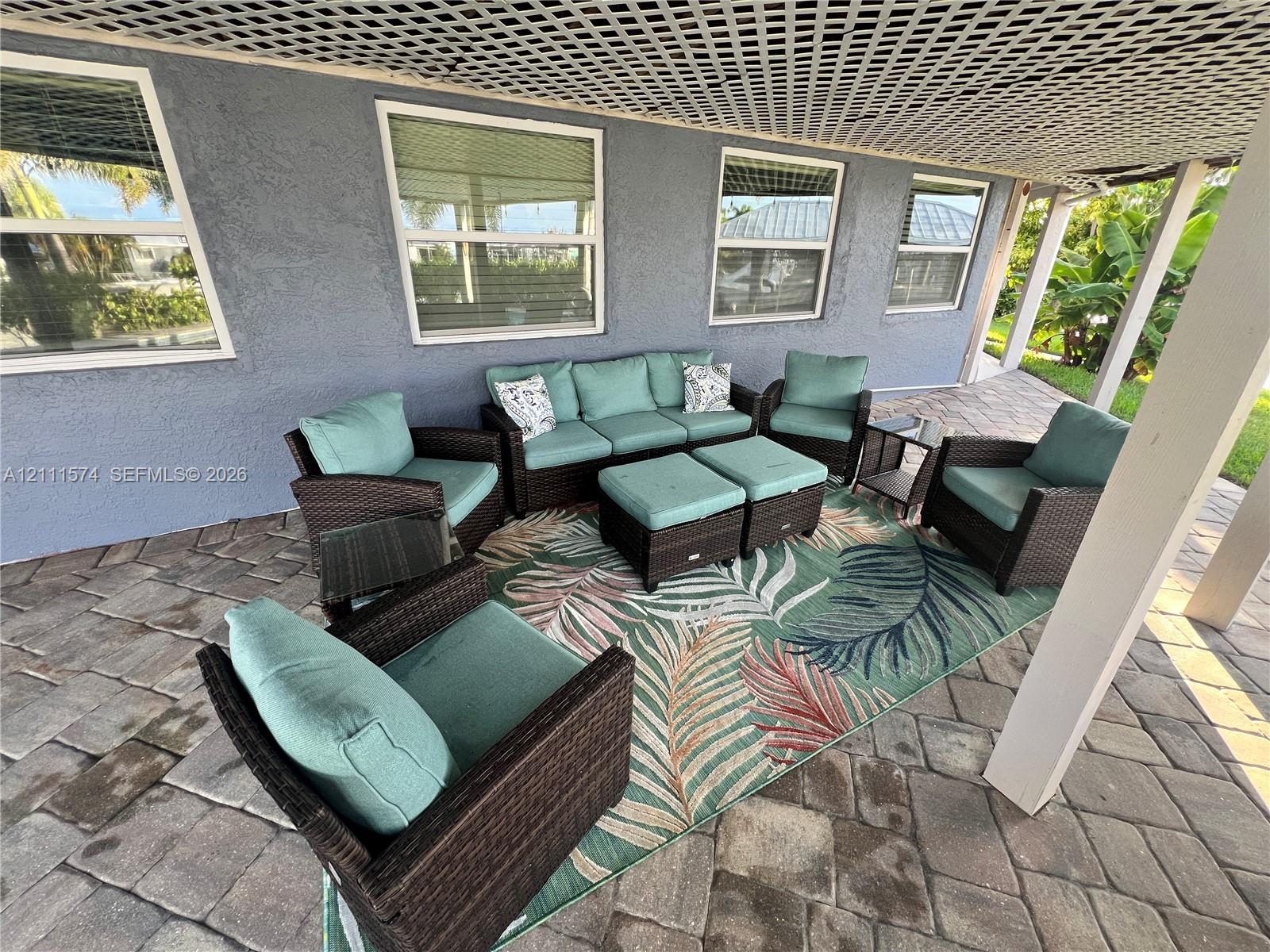 Covered patio featuring concrete paver flooring, stucco exterior walls, multi-pane windows, and a decorative lattice ceiling treatment