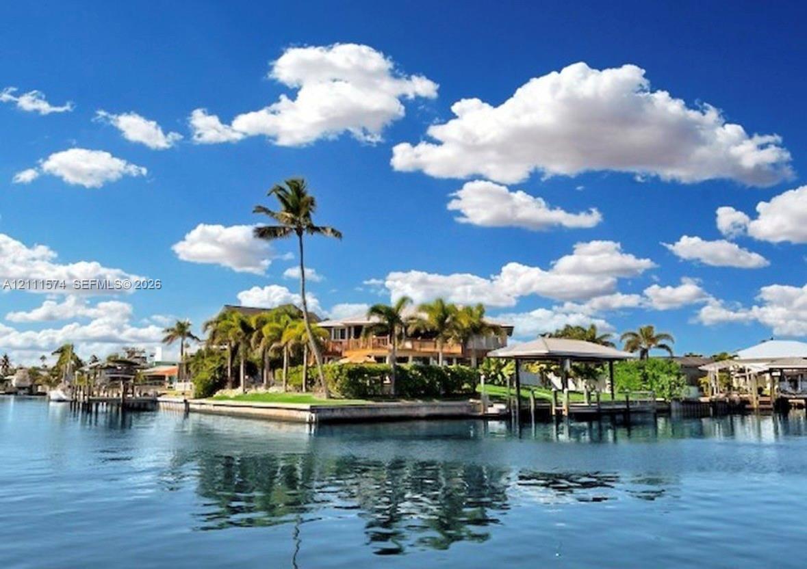 Waterfront residence featuring a private boat dock, covered boat slip, mature palm trees, and manicured landscaping