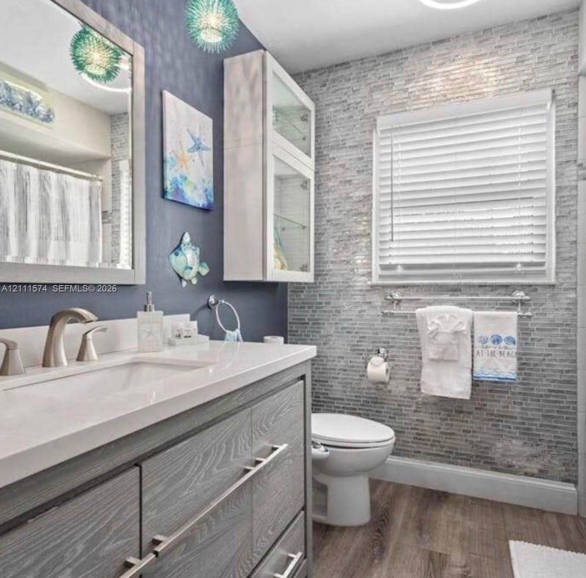 Vanity featuring a stone-finish countertop, undermount sink, and wood-finish cabinetry with brushed metal pulls