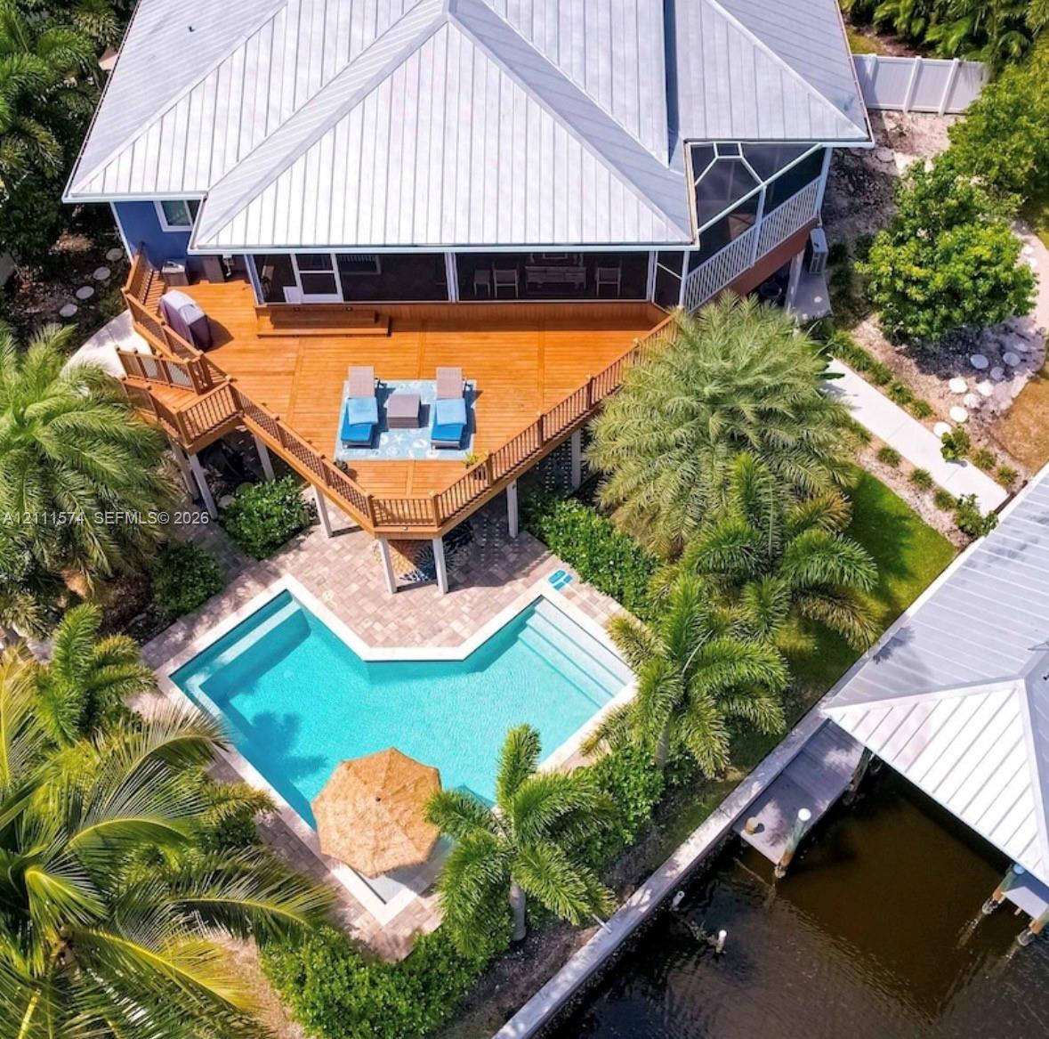 Aerial perspective featuring a multi-level wood deck, swimming pool with paver surround, and private boat dock with metal roof Aerial perspective featuring a multi-level wood deck, swimming pool with paver surround, and private boat dock with metal roof
