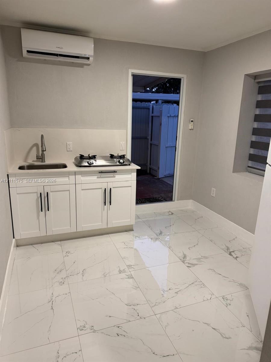 Kitchenette featuring white cabinetry with dark hardware, stone-surface countertops, a stainless steel sink with a high-arch faucet, a dual-burner cooktop, and large-format tile flooring