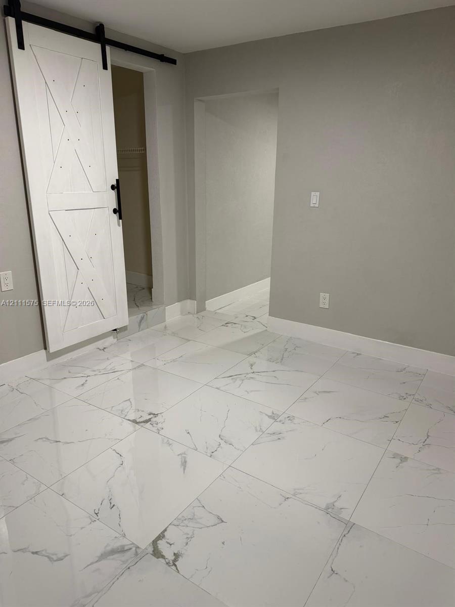Large-format polished tile flooring featuring a grey-vein pattern, white wood-finish sliding barn door with black iron hardware, and neutral wall tones