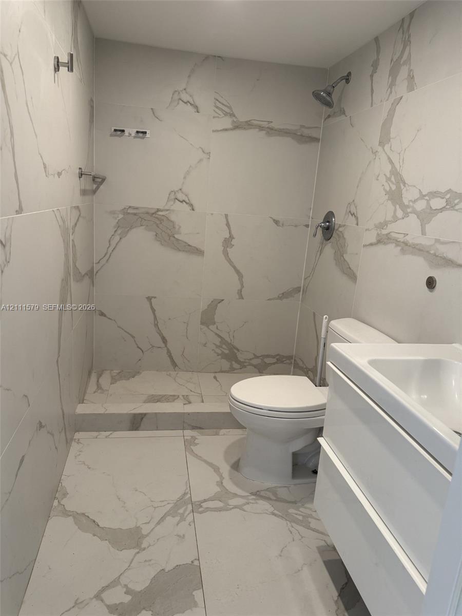 Walk-in shower enclosure featuring large-format stone-patterned tile, white floating vanity, and chrome fixtures