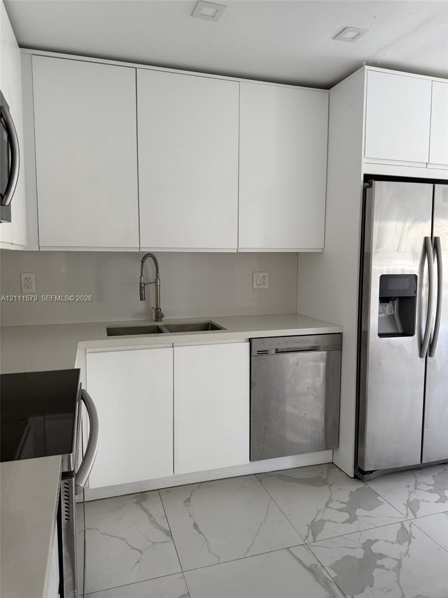 Modern kitchen featuring flat-panel white cabinetry, solid-surface countertops, recessed ceiling lighting, stainless steel appliances, and large-format tile flooring