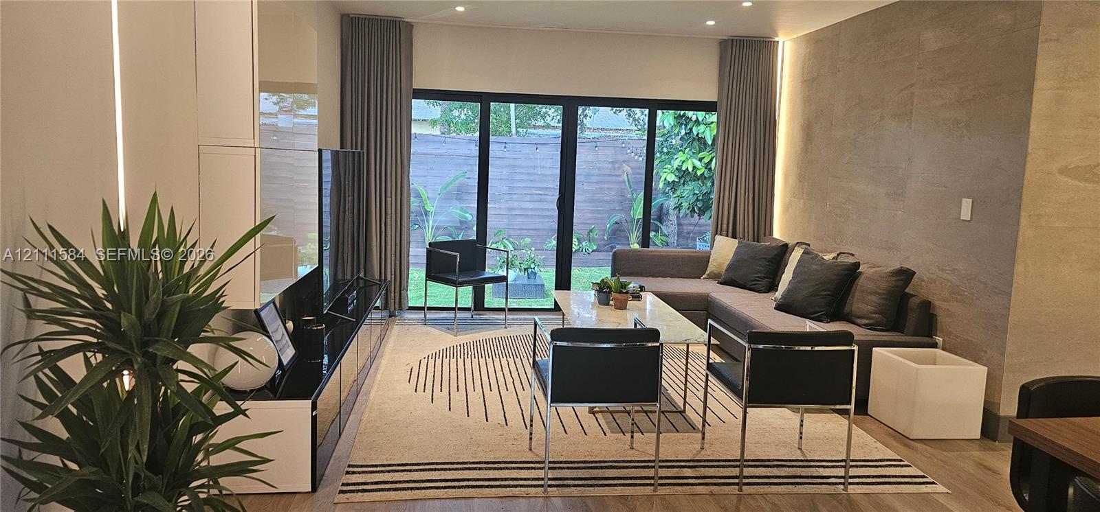 Floor-to-ceiling multi-panel glass doors, recessed ceiling lighting, vertical LED wall accent, stone-finish feature wall, and wood-finish flooring