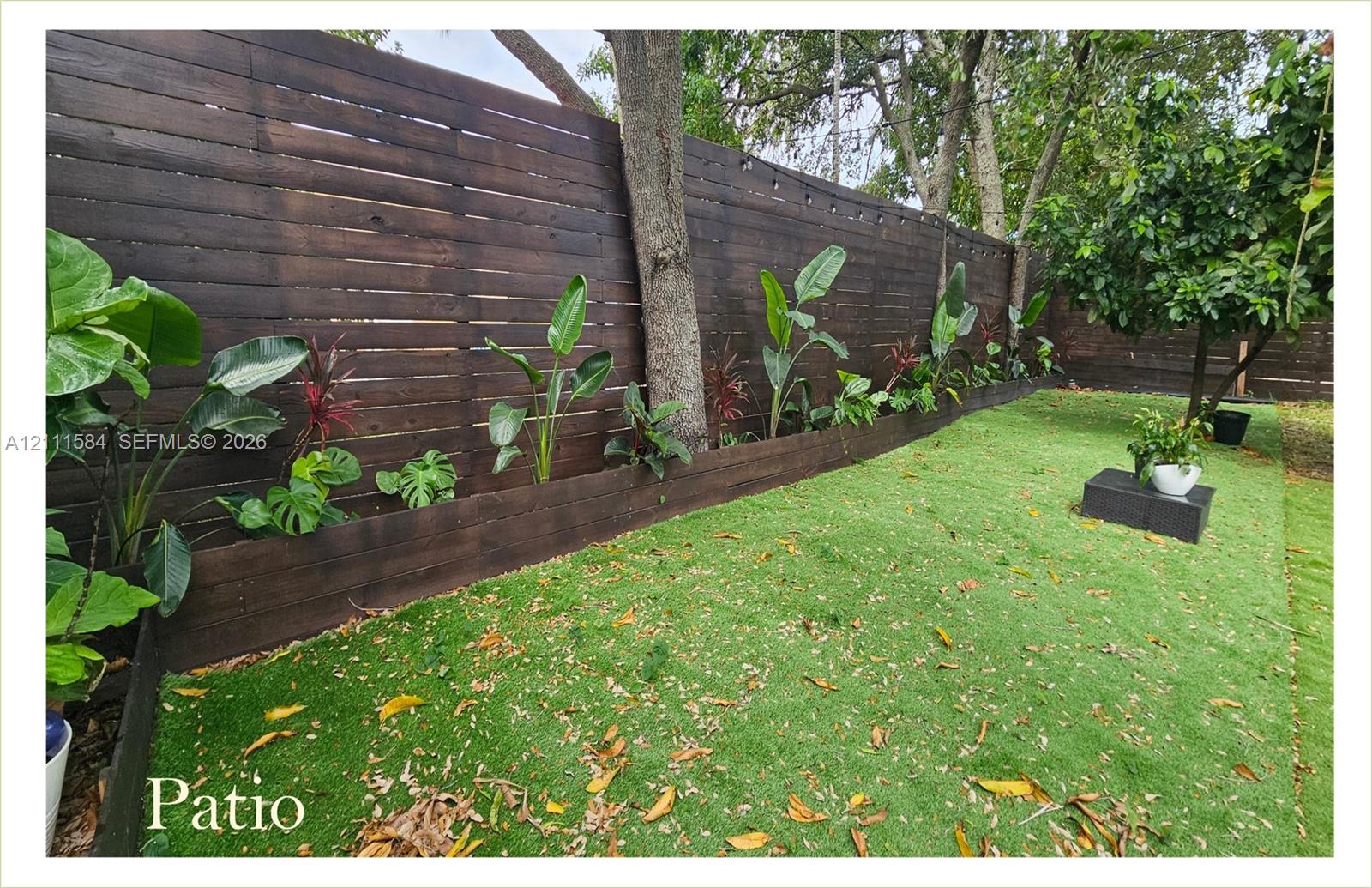 Horizontal dark-stained wood slat fencing, artificial turf lawn, raised wood garden bed border, and mature trees