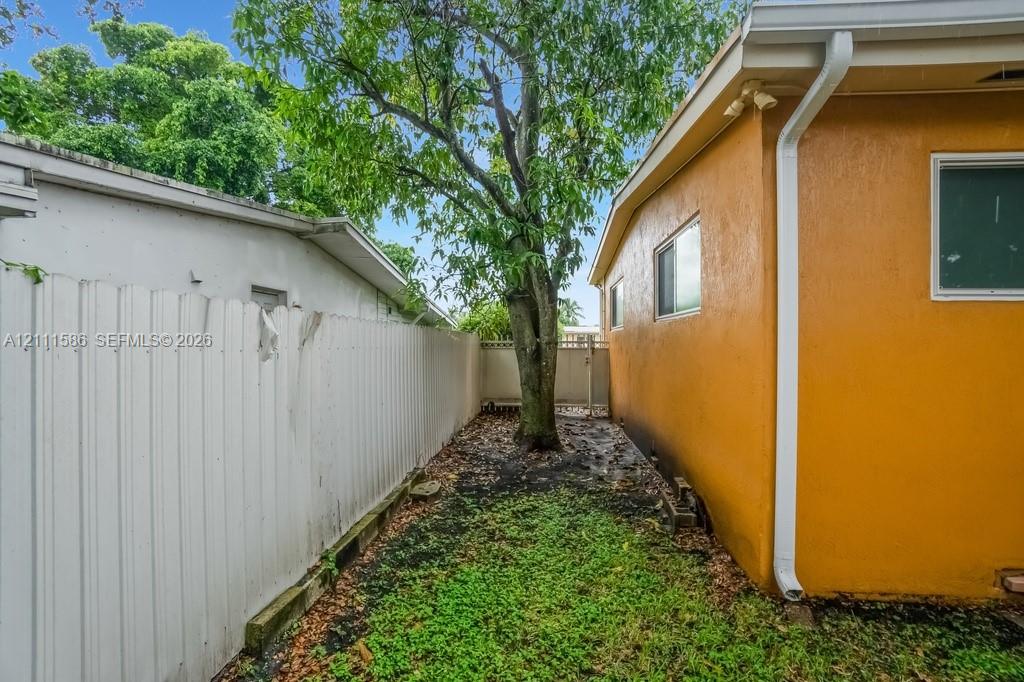Side yard featuring a stucco exterior, white vinyl privacy fencing, integrated gutter system, and mature tree canopy