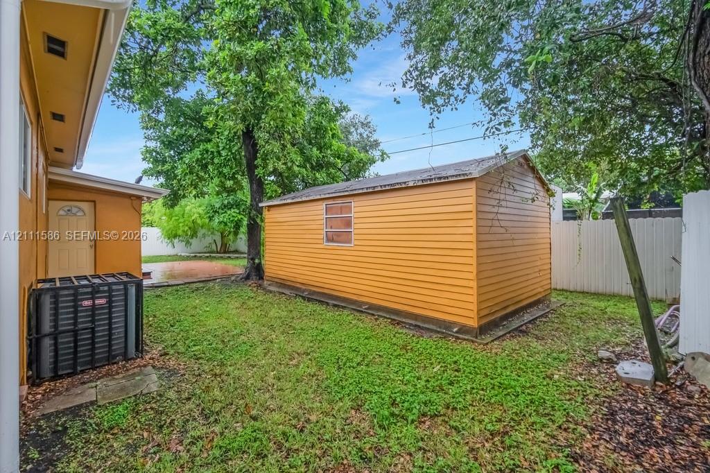 Backyard area featuring a detached storage structure with horizontal siding, a fenced perimeter, and mature trees