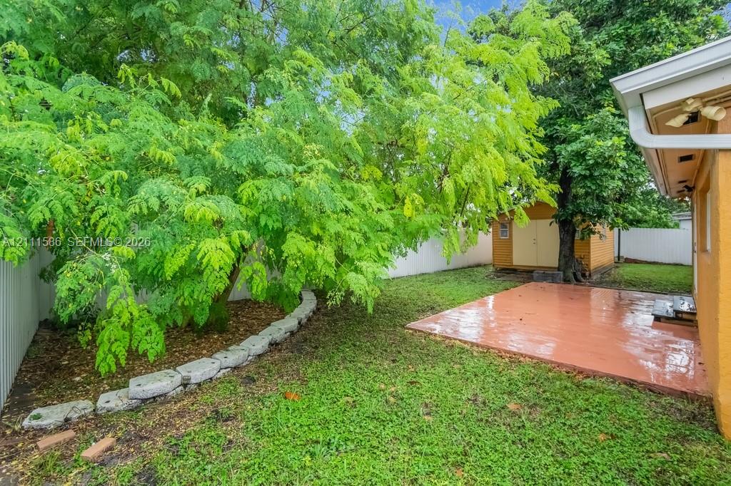 Rear yard featuring a paved patio, detached storage structure, stone garden edging, and mature trees enclosed by privacy fencing