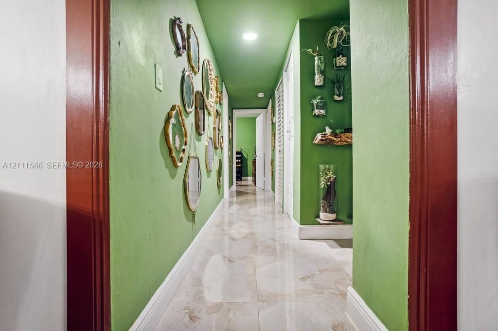 Hallway featuring large-format polished tile flooring, recessed ceiling lighting, and custom millwork door casings finished in a deep red tone