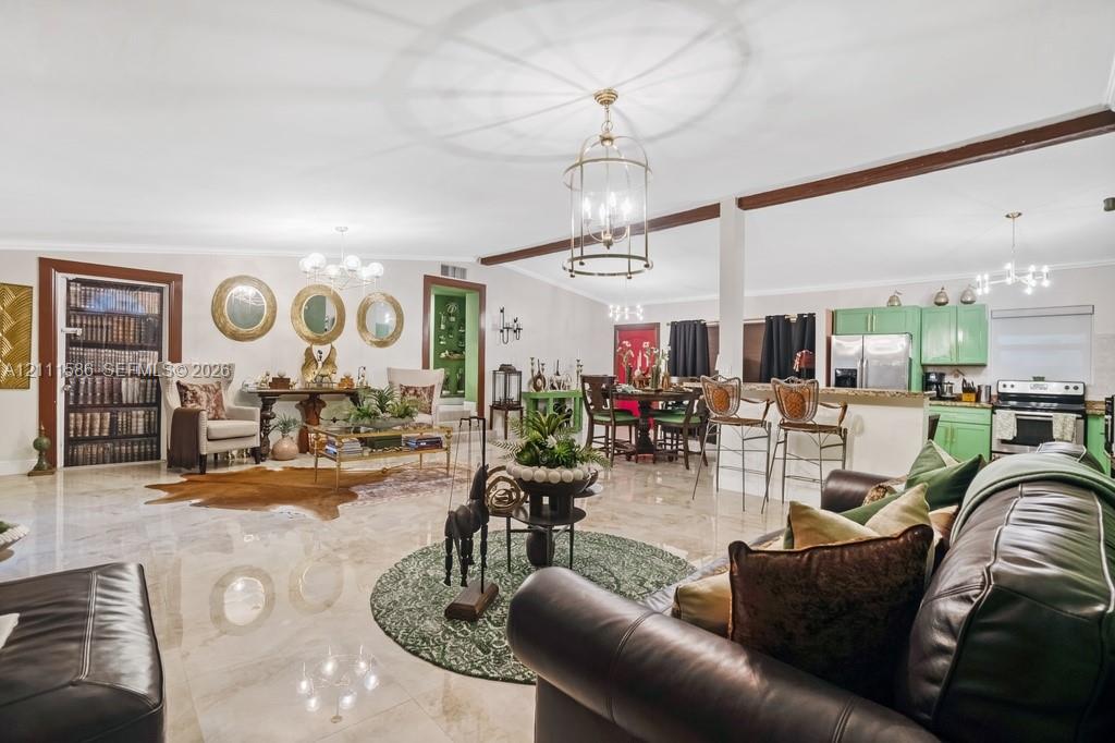 Open-concept interior featuring large-format tile flooring, exposed ceiling beams, custom green cabinetry, stone-surface breakfast bar, and ornate multi-light pendant fixtures