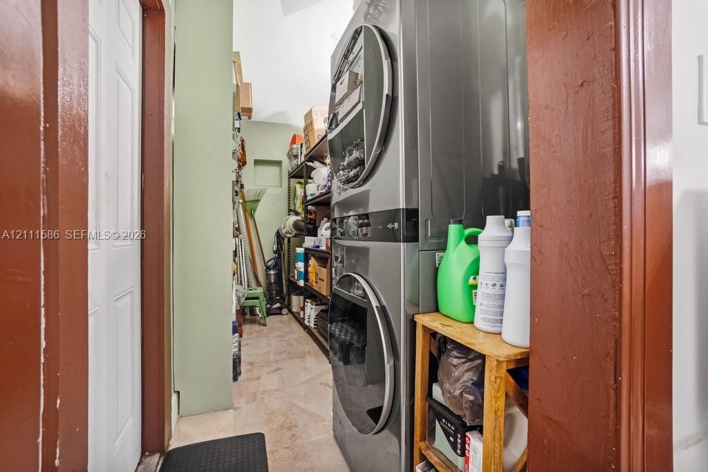 Utility space featuring stacked laundry appliances and tile flooring