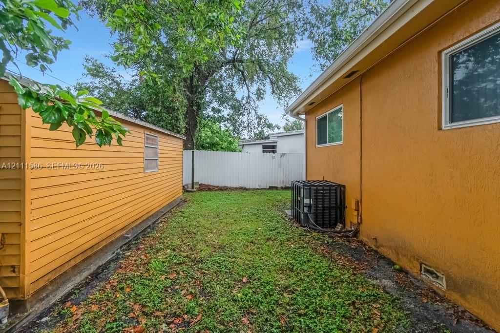 Exterior side yard featuring a stucco-finish wall, horizontal-siding storage structure, and vinyl privacy fencing