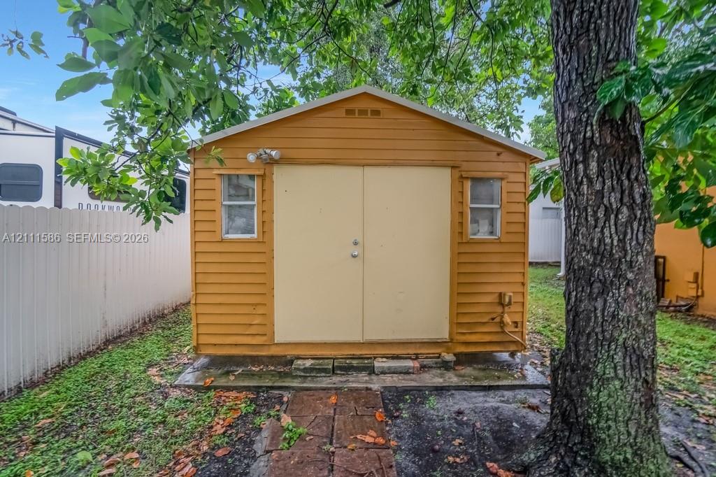 Detached storage shed featuring horizontal lap siding, double doors, dual windows, and an exterior light fixture, set on a stone paver path