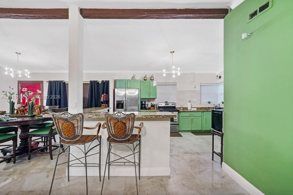 Kitchen featuring cabinetry with matte green finish, stone-surfaced countertops, exposed wood ceiling beams, polished tile flooring, and multiple multi-arm pendant light fixtures