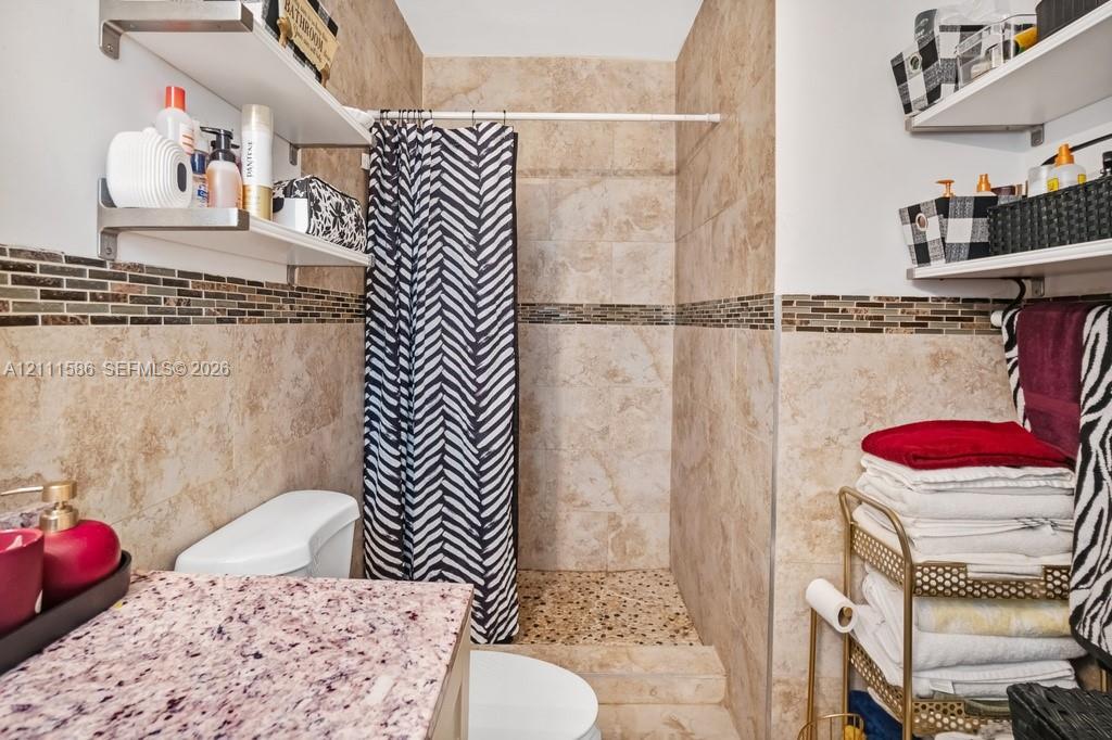 Bathroom featuring large-format tile wall cladding, glass and stone mosaic tile accents, a walk-in shower with pebble-stone flooring, and floating wall-mounted shelving