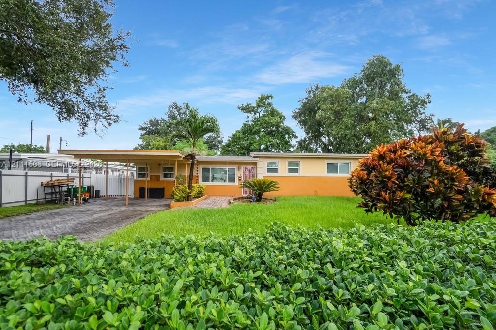 Single-story residence featuring a two-tone exterior, attached carport, paver driveway, manicured lawn, and privacy fencing