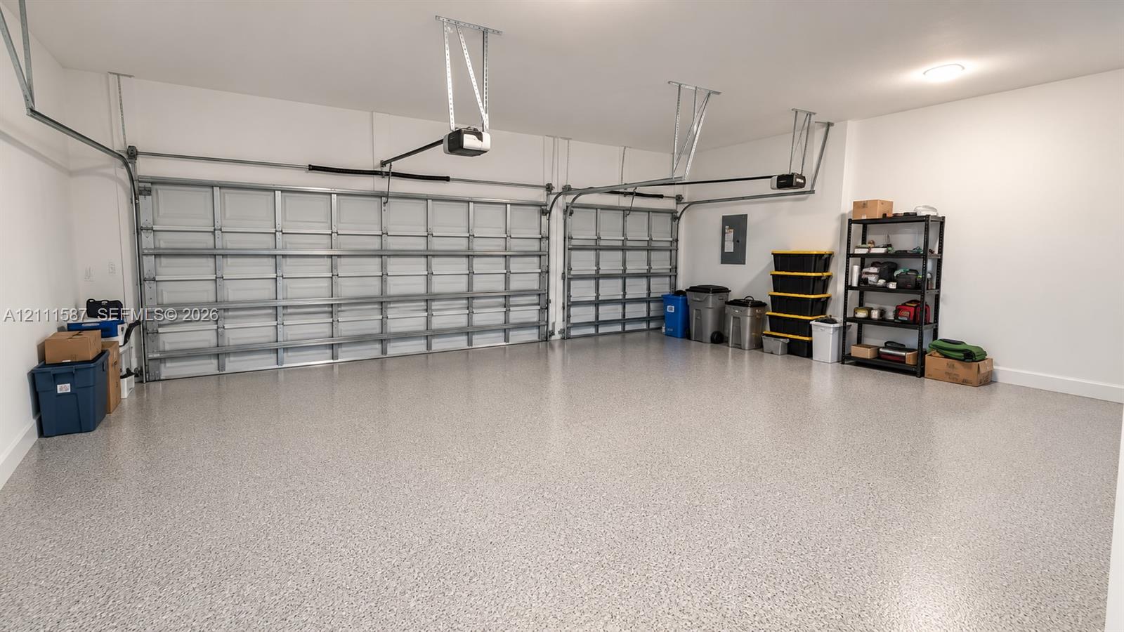 Three-car garage featuring a speckled epoxy floor coating, two paneled overhead doors, and dual garage door openers