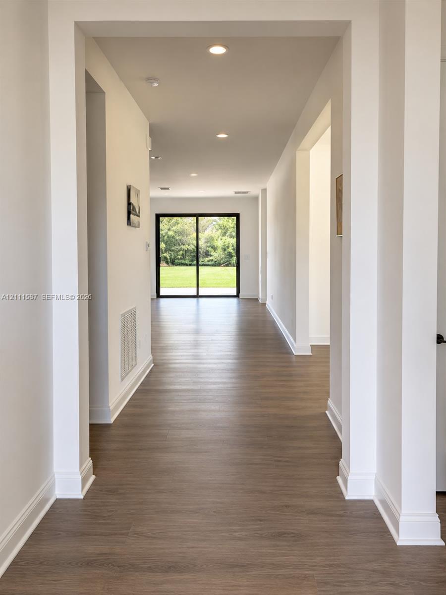 Interior corridor featuring wood-finish flooring, recessed ceiling lighting, and black-framed sliding glass doors opening to an exterior green space