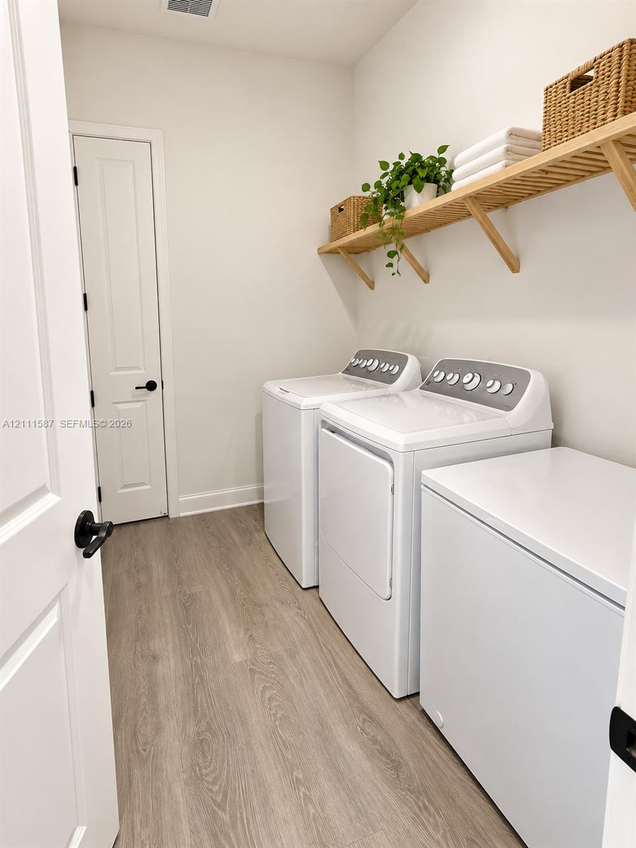 Laundry room featuring wood-finish flooring, a wall-mounted wood shelf, and a white six-panel interior door with matte black hardware