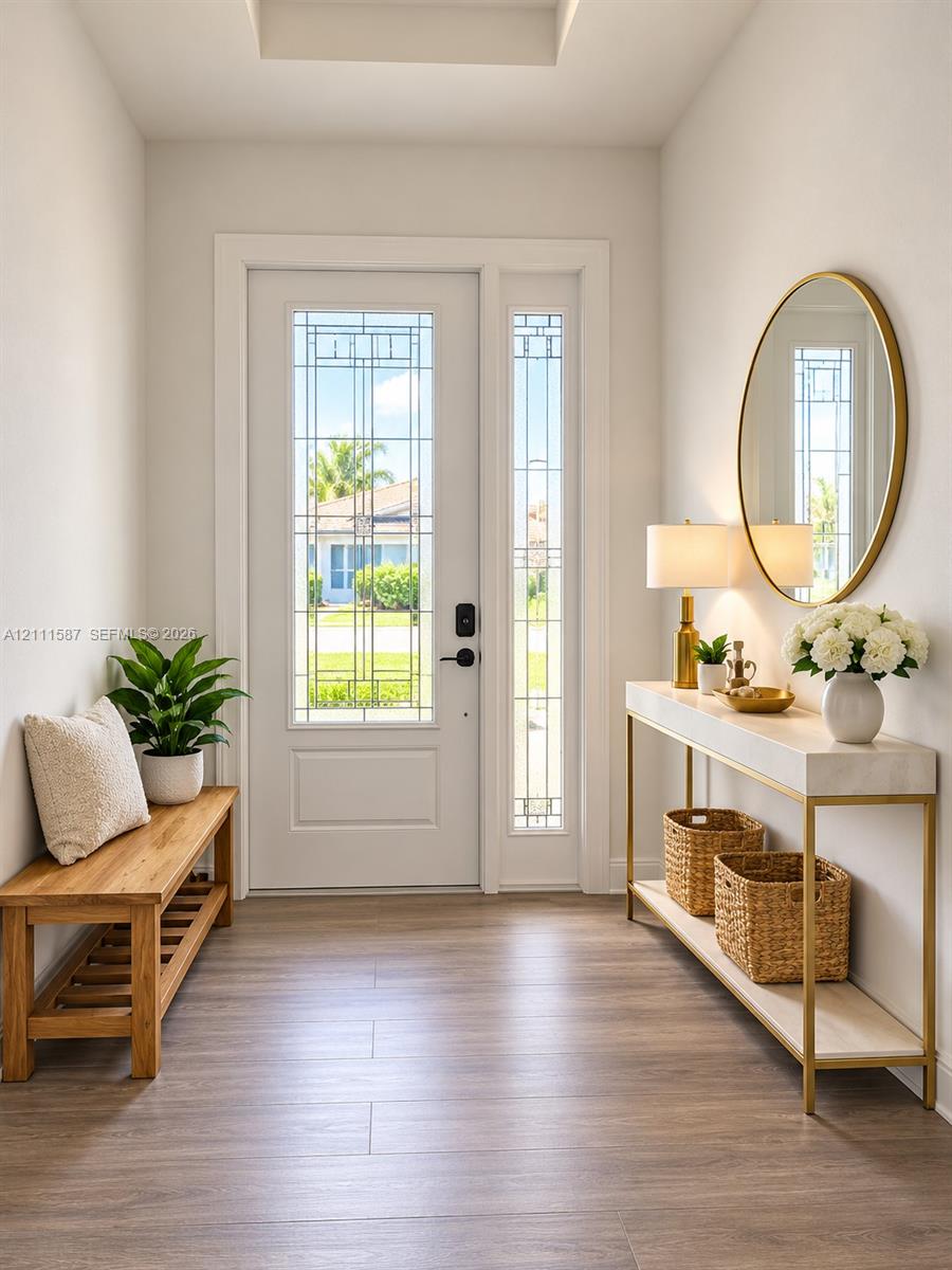 Entryway featuring wood-finish flooring, a recessed tray ceiling, and a white exterior door with integrated geometric glass paneling and a side light