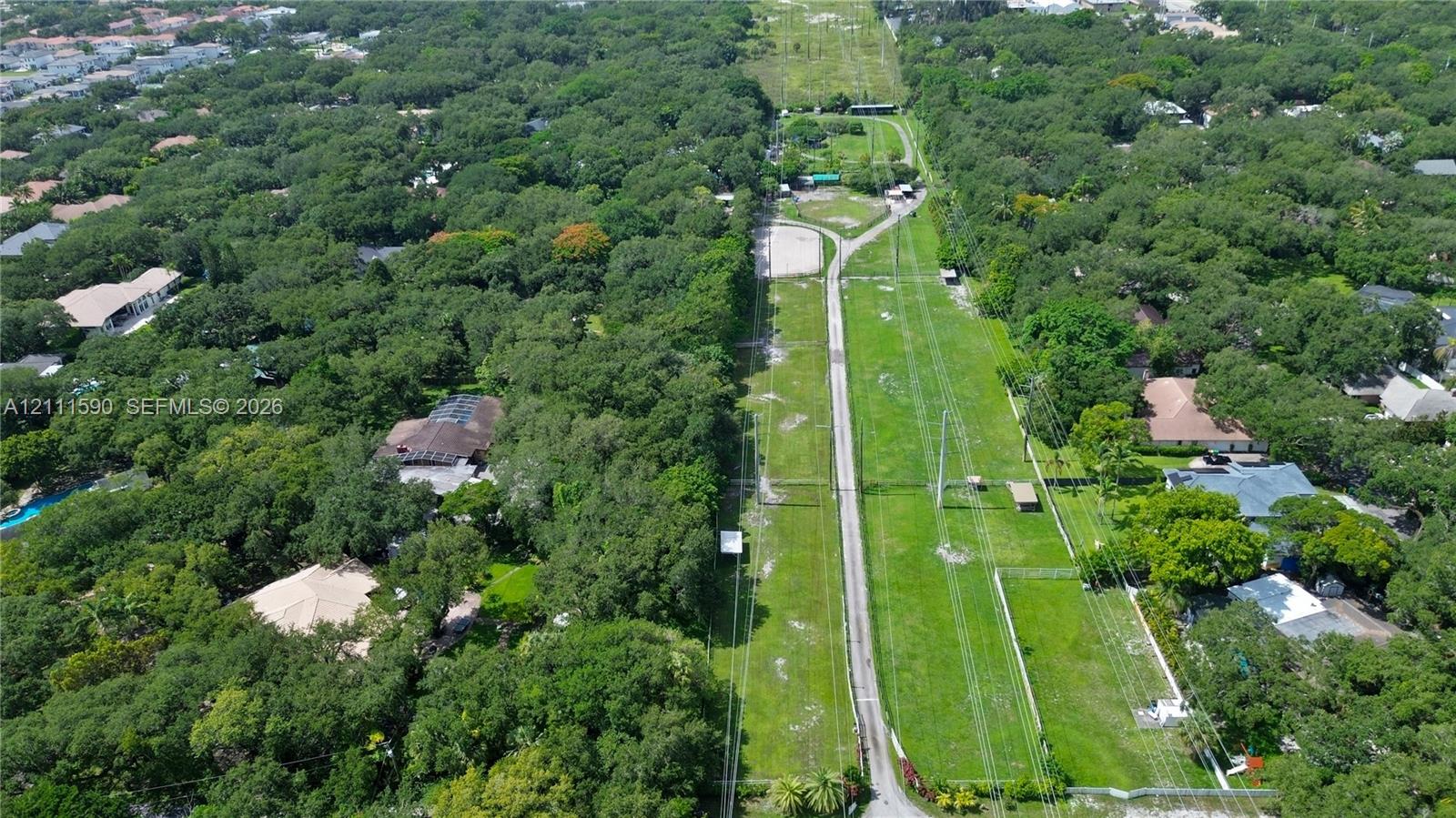Aerial view of an expansive parcel featuring dense tree coverage, a linear stretch of open green space, and a paved path