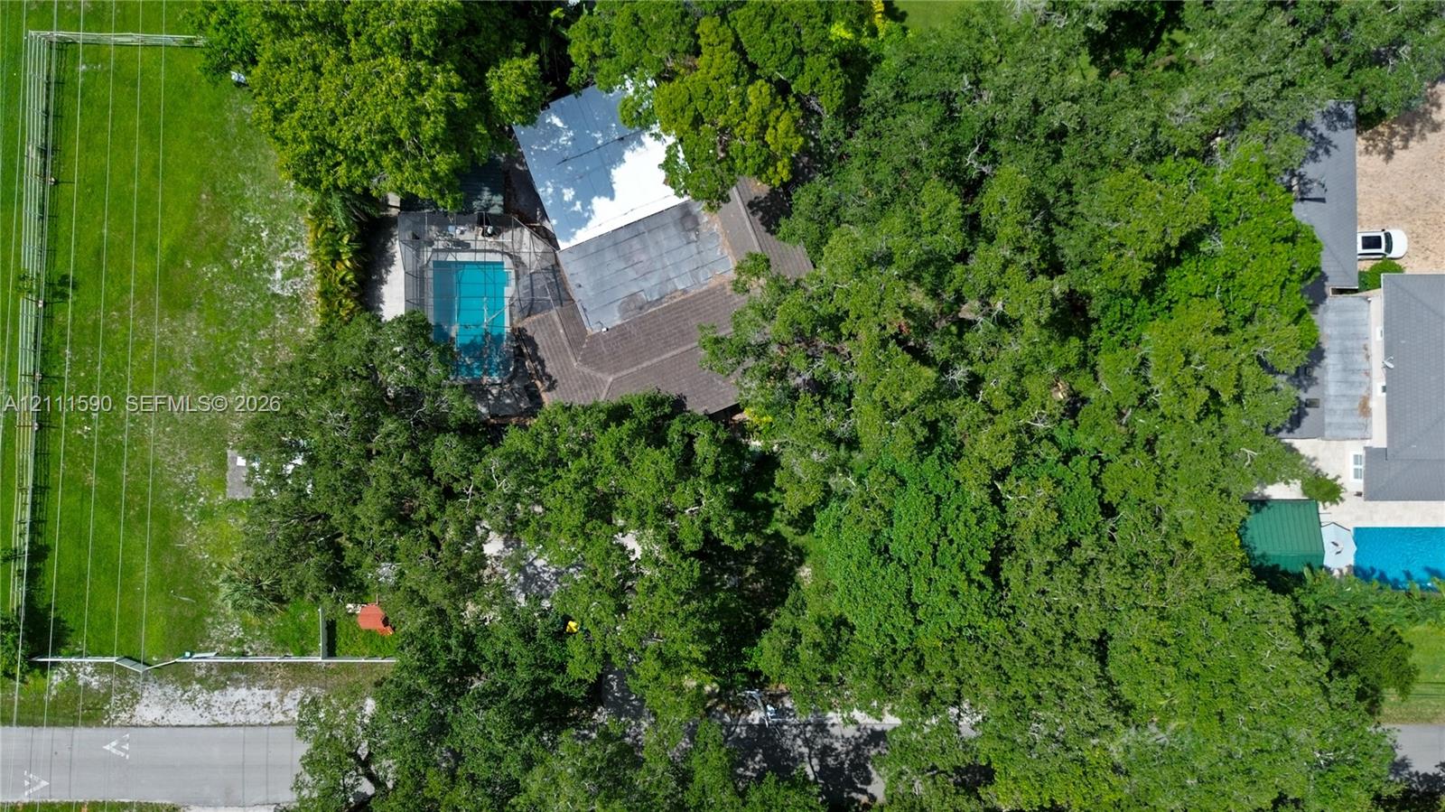 Aerial perspective featuring an expansive lot, mature tree canopy, fenced perimeter, and an in-ground pool with a screen enclosure