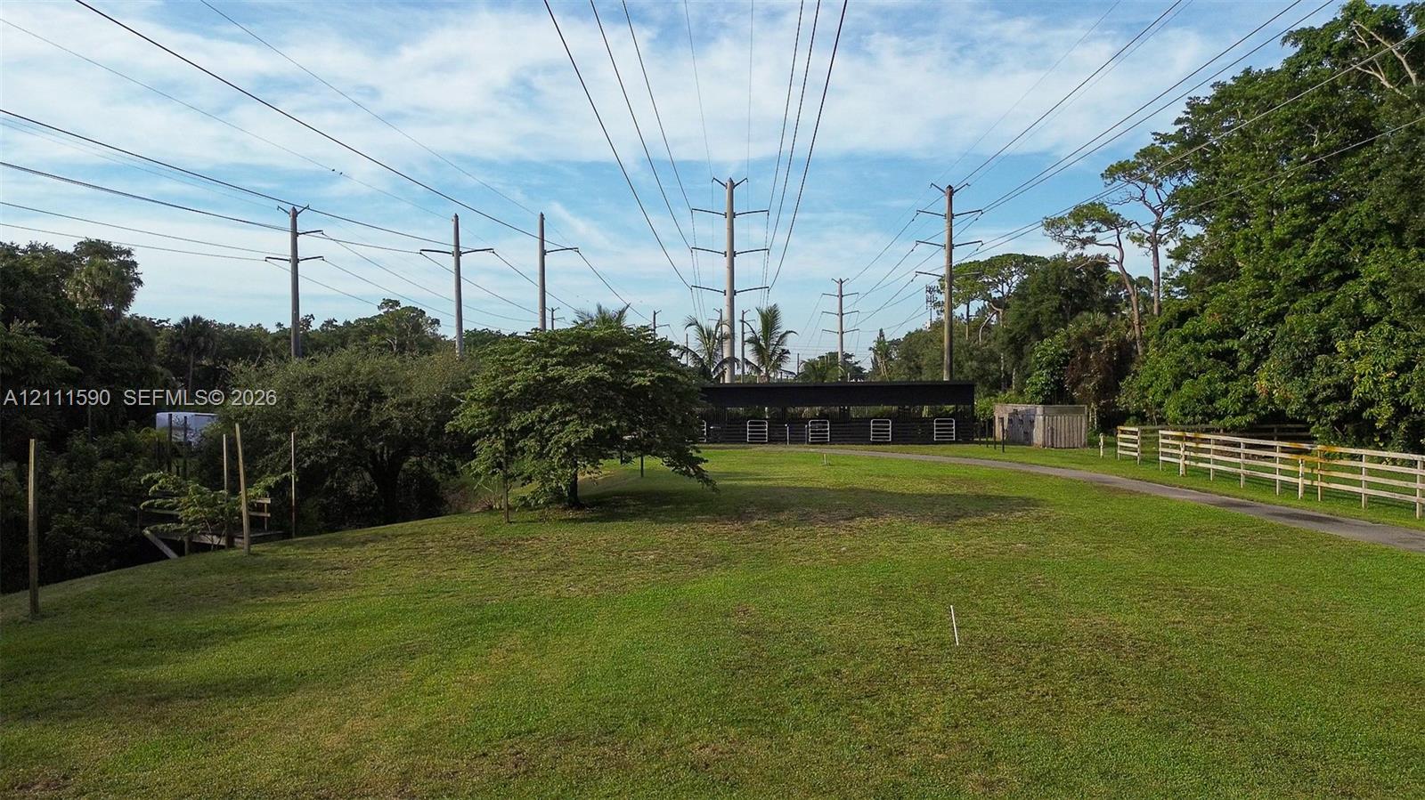 Expansive lot featuring a manicured lawn, mature trees, and white post-and-rail fencing