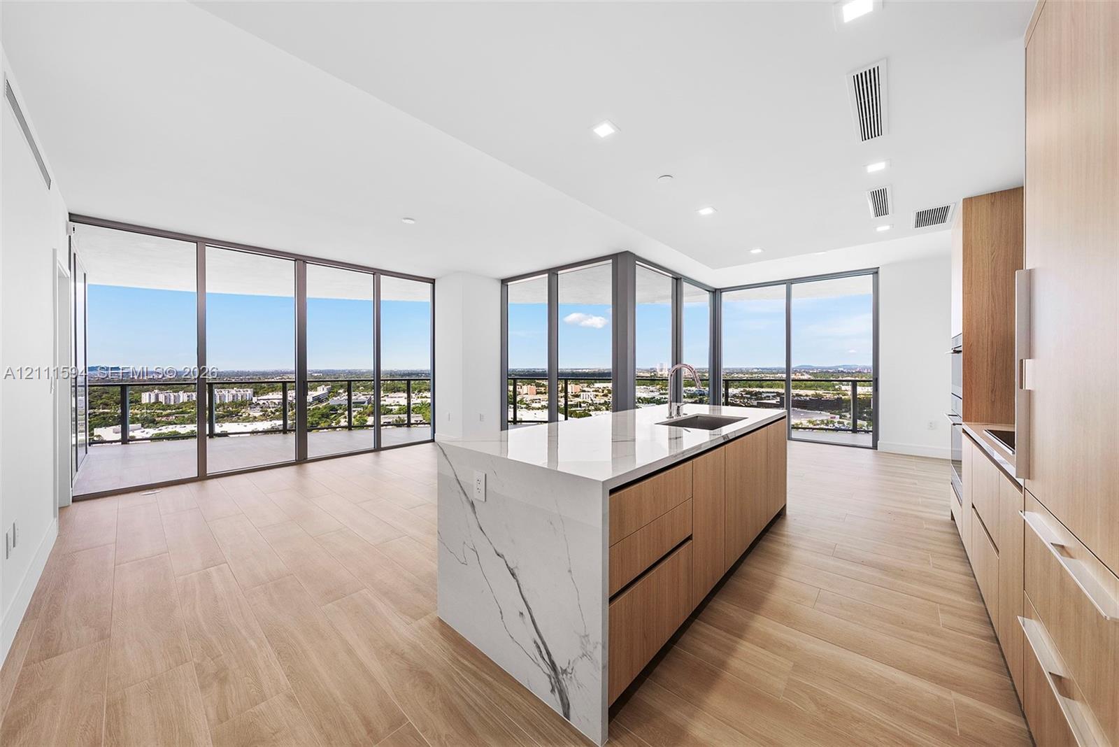 Kitchen featuring wood-finish cabinetry, an island with a stone-surface countertop, floor-to-ceiling glass panel walls, and wood-finish flooring Kitchen featuring wood-finish cabinetry, an island with a stone-surface countertop, floor-to-ceiling glass panel walls, and wood-finish flooring