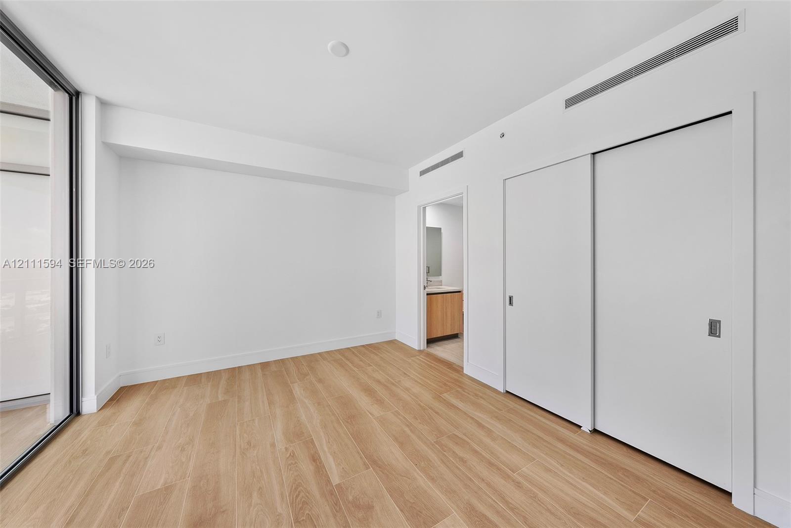 Room featuring wood-finish flooring, full-height sliding door closet, floor-to-ceiling glass wall, and smooth-finish white walls