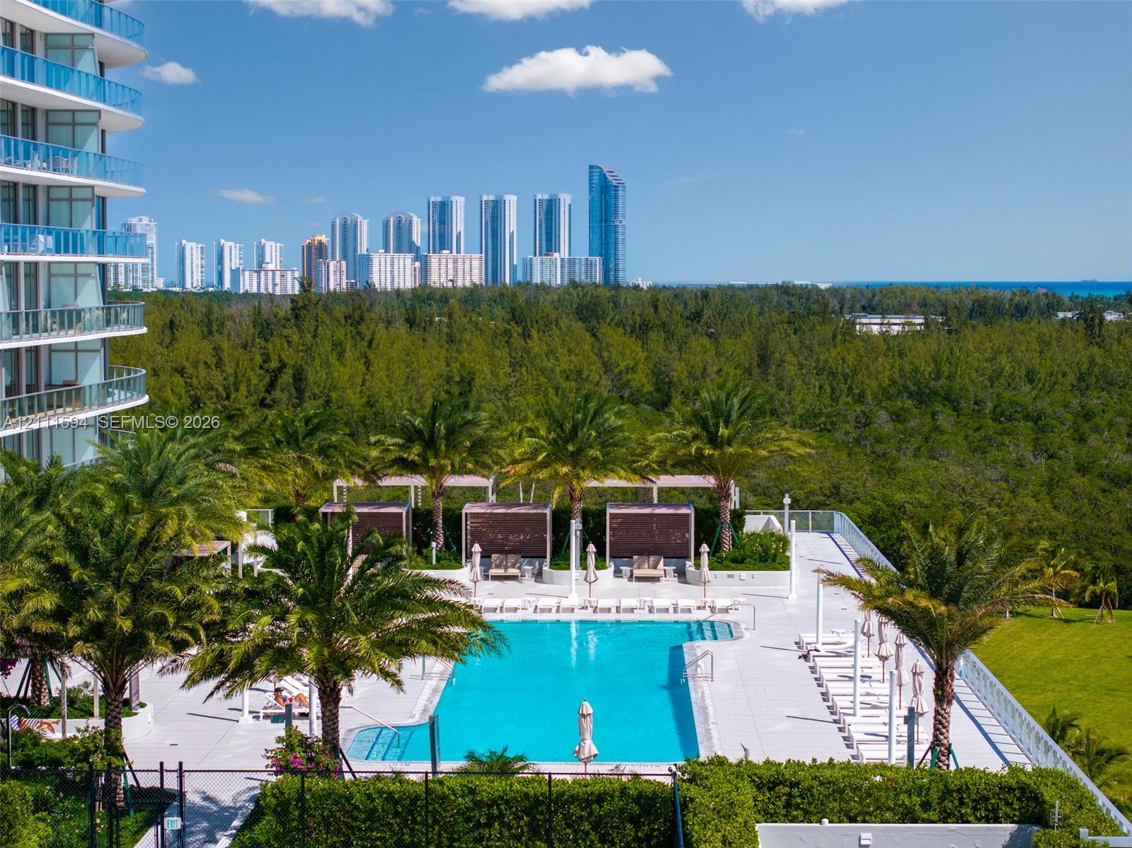 Swimming pool with concrete decking, perimeter privacy hedging, mature palm trees, and elevated cabanas