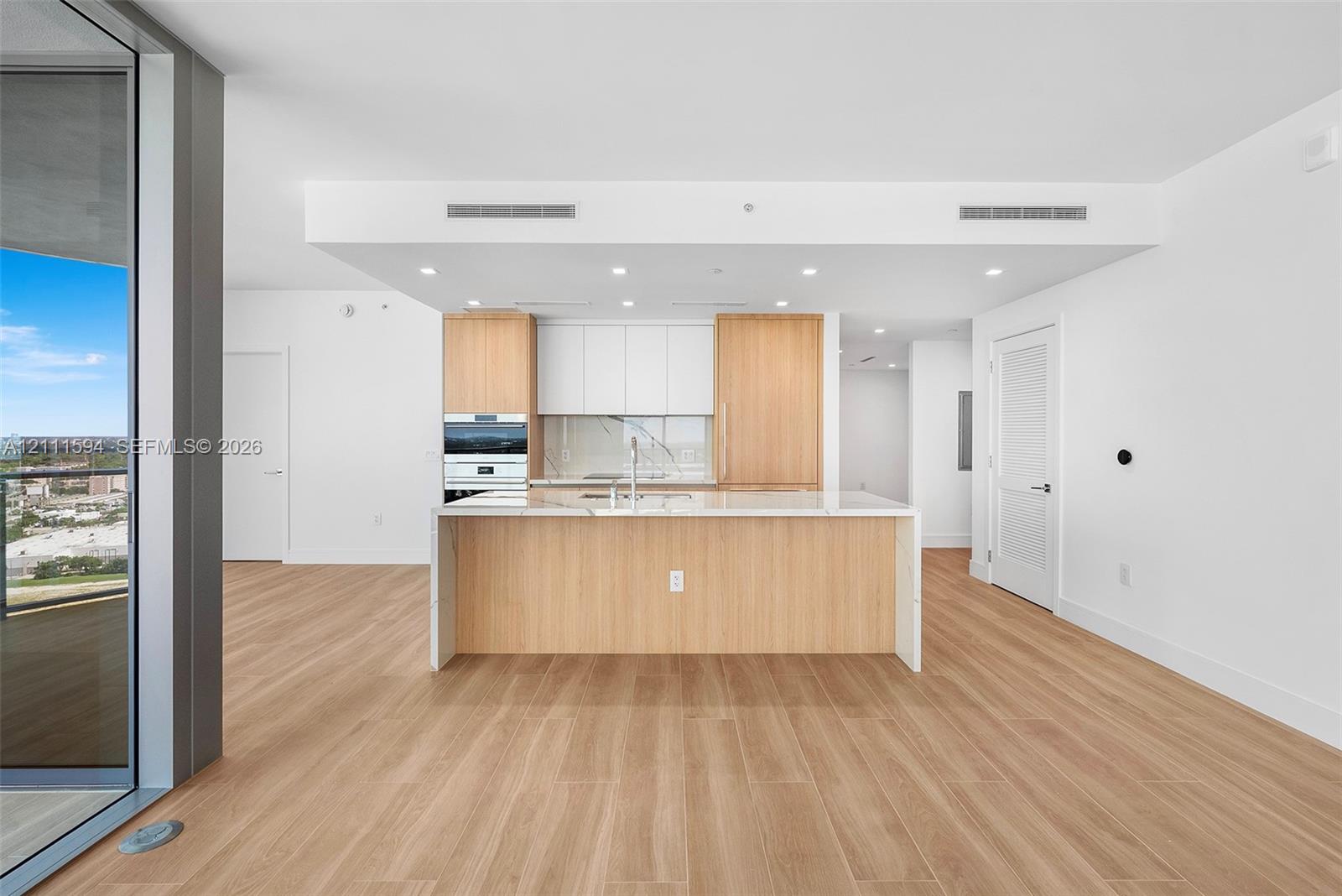Kitchen featuring wood-finish cabinetry, white slab countertops, a central island, recessed lighting, and integrated wall oven