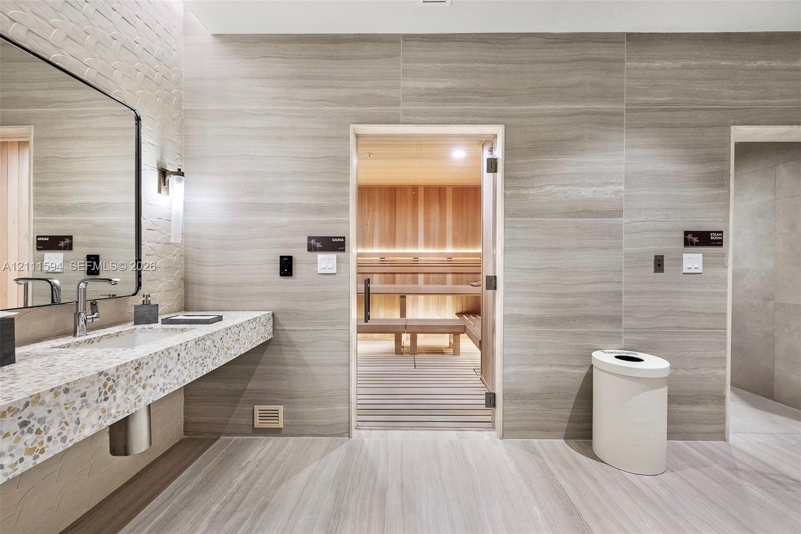 Sauna room featuring cedar wood wall paneling and tiered bench seating, complemented by a stone-tiled accent wall, a floating vanity with a terrazzo-style countertop, and a large wall-mounted mirror