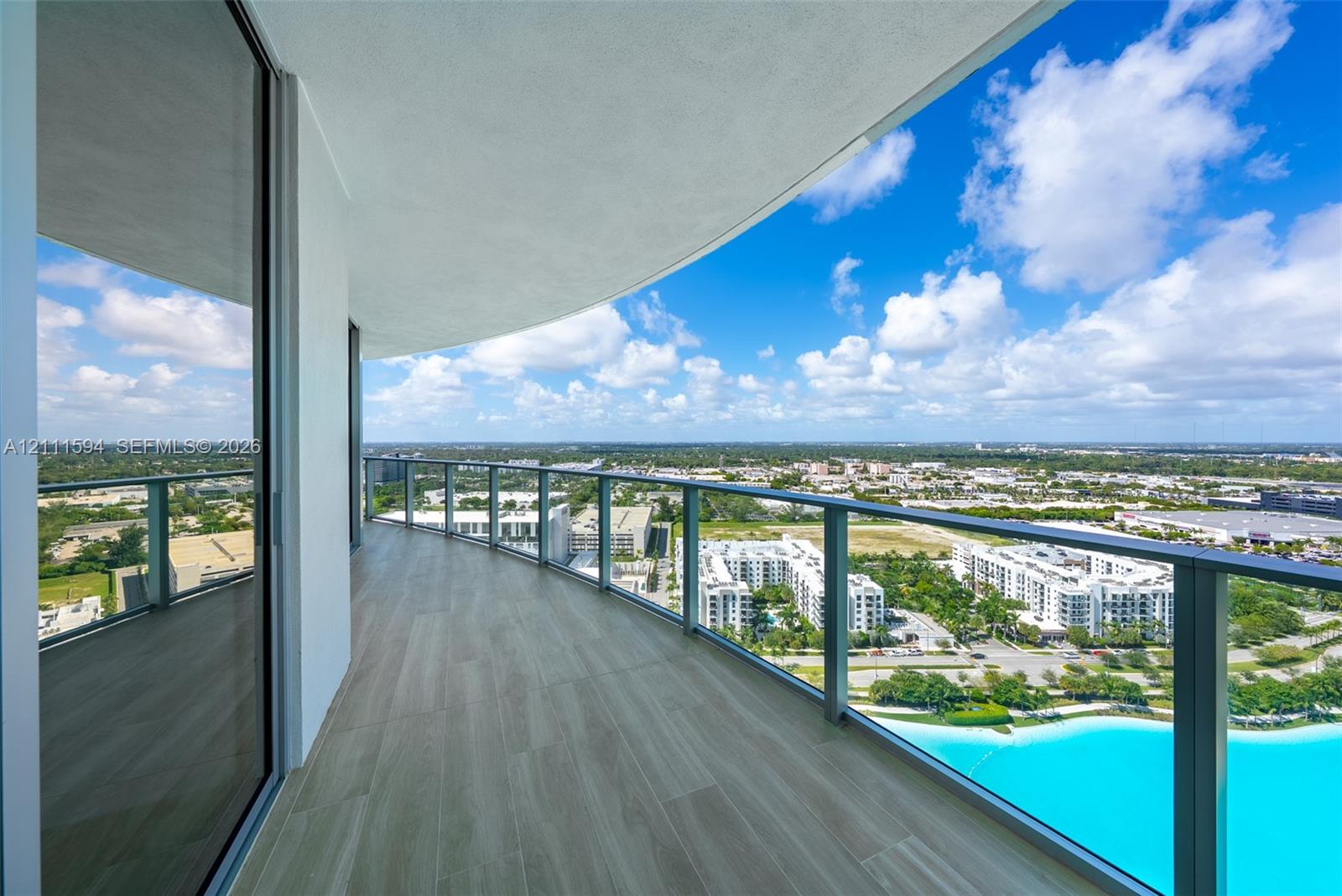 Curved balcony featuring wood-finish tile flooring, a glass panel railing, and expansive exterior scenery