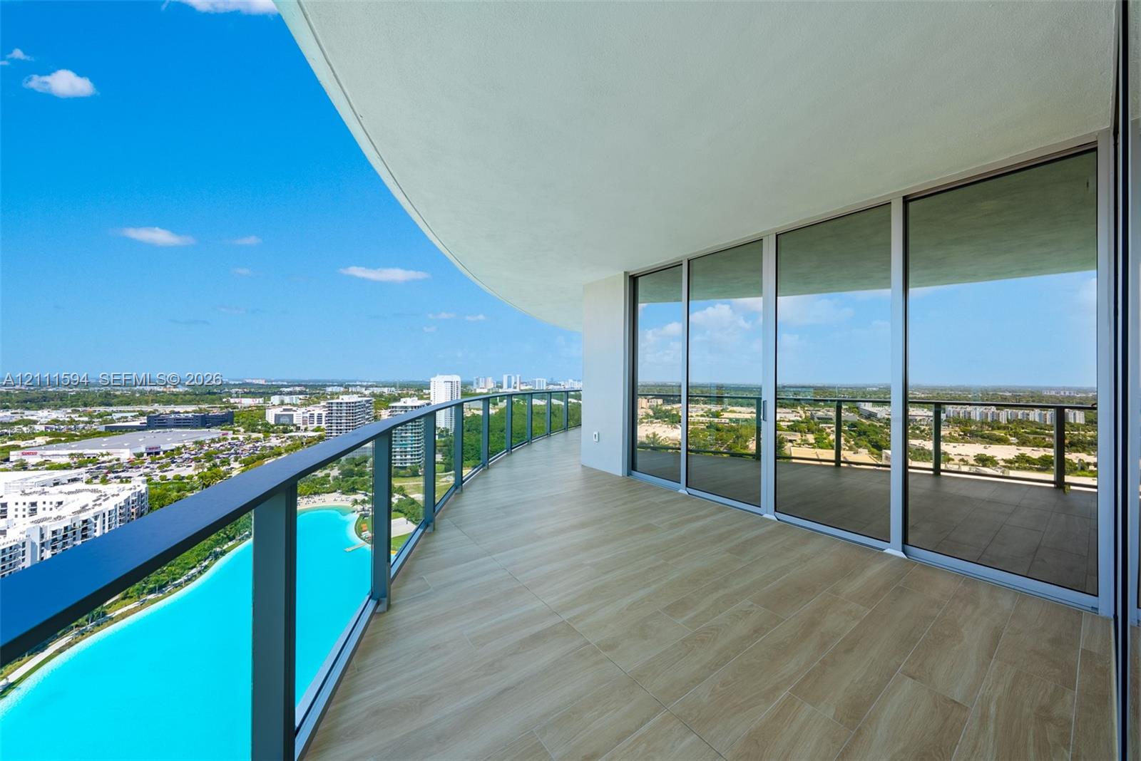 Expansive covered balcony featuring tile flooring, metal railing, and floor-to-ceiling glass panel doors
