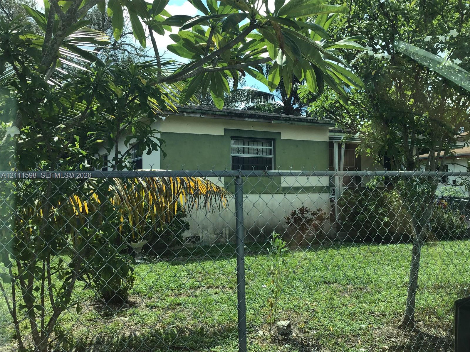 Single-story residence featuring a two-tone exterior facade, metal window security bars, and a chain-link perimeter fence Single-story residence featuring a two-tone exterior facade, metal window security bars, and a chain-link perimeter fence
