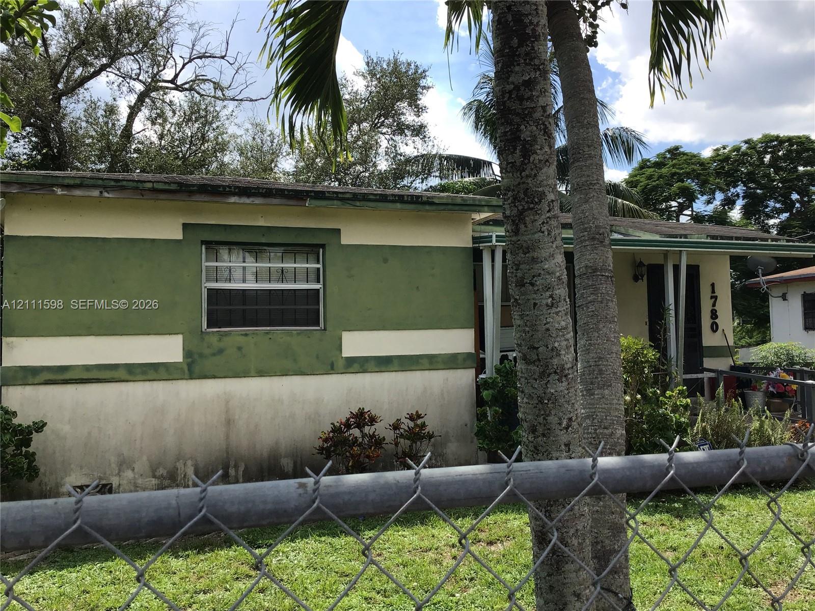 Single-story exterior featuring a painted stucco facade, metal-framed windows, a covered front entryway, and mature palm trees Single-story exterior featuring a painted stucco facade, metal-framed windows, a covered front entryway, and mature palm trees
