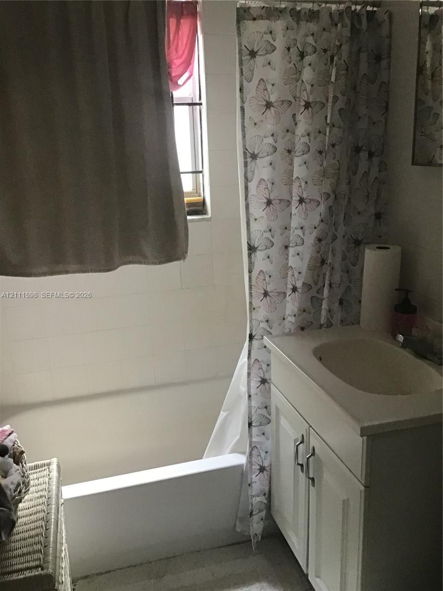 Bathroom featuring a porcelain tub with white tiled wall surround, single-basin vanity with cabinet storage, and window with muntins