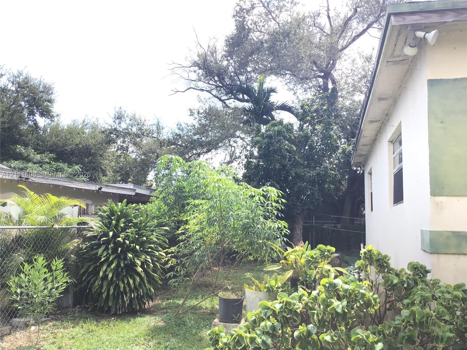 Exterior featuring a light-colored smooth stucco finish, mature trees, expansive shrubbery, and chain-link fencing Exterior featuring a light-colored smooth stucco finish, mature trees, expansive shrubbery, and chain-link fencing