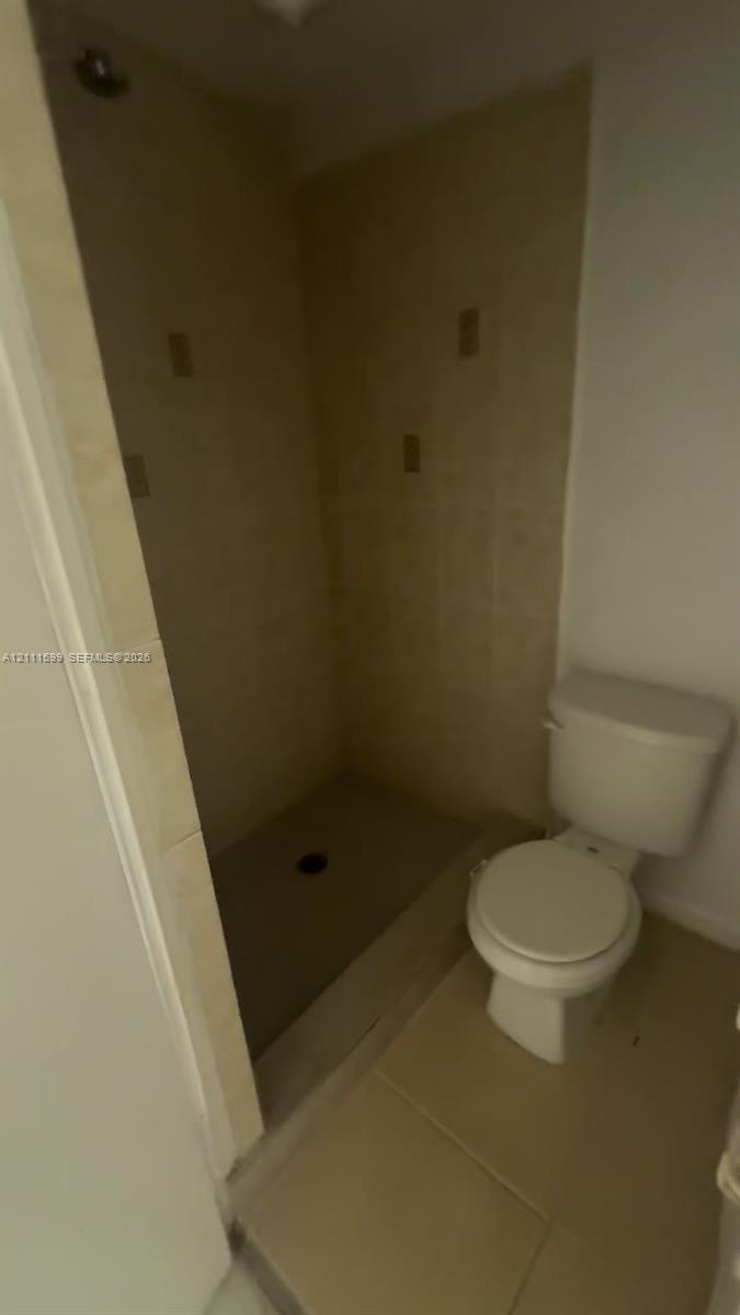 Walk-in shower with neutral tile surround, overhead shower head, and floor-mounted toilet